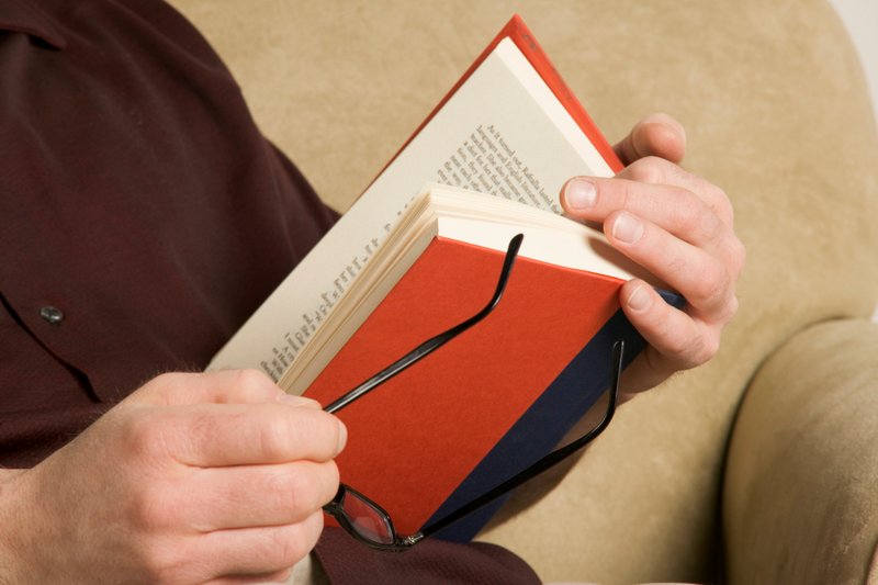 Homem segurando o livro e óculos